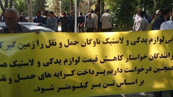 Truck drivers hold a banner that reads the high cost of spare parts are breaking the backs of the drivers